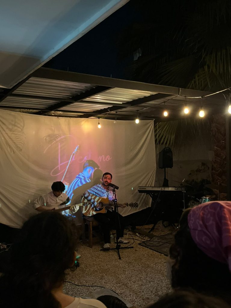 Concierto en vivo en Relato: cantante con guitarra acústica frente a proyección Destino