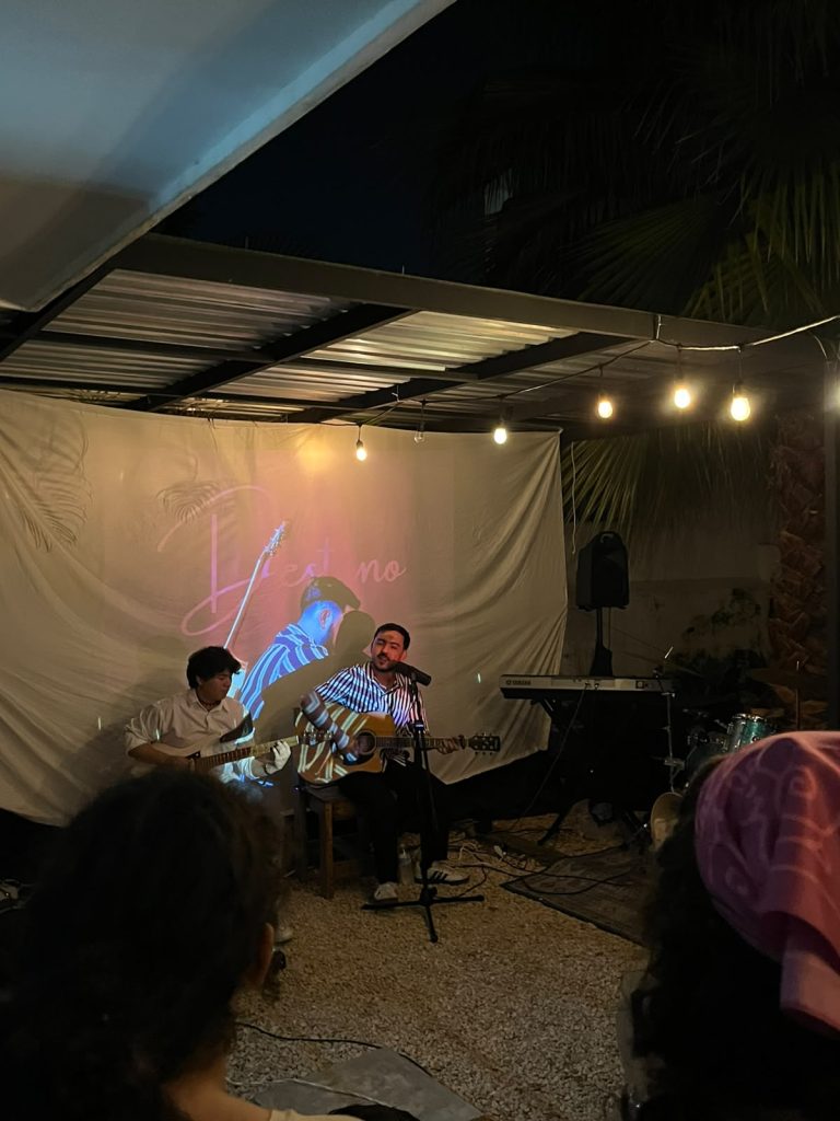 Dos músicos toca guitarra en vivo bajo luces cálidas en el patio de Relato